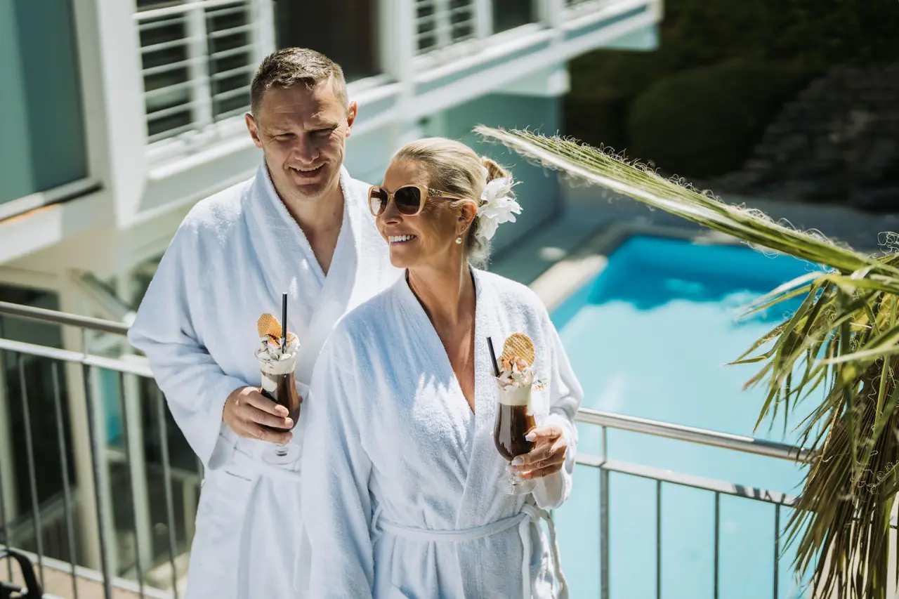 Glückliches Paar in Bademänteln mit erfrischenden Getränken am Poolbereich des Kurhotel Sonnenhof