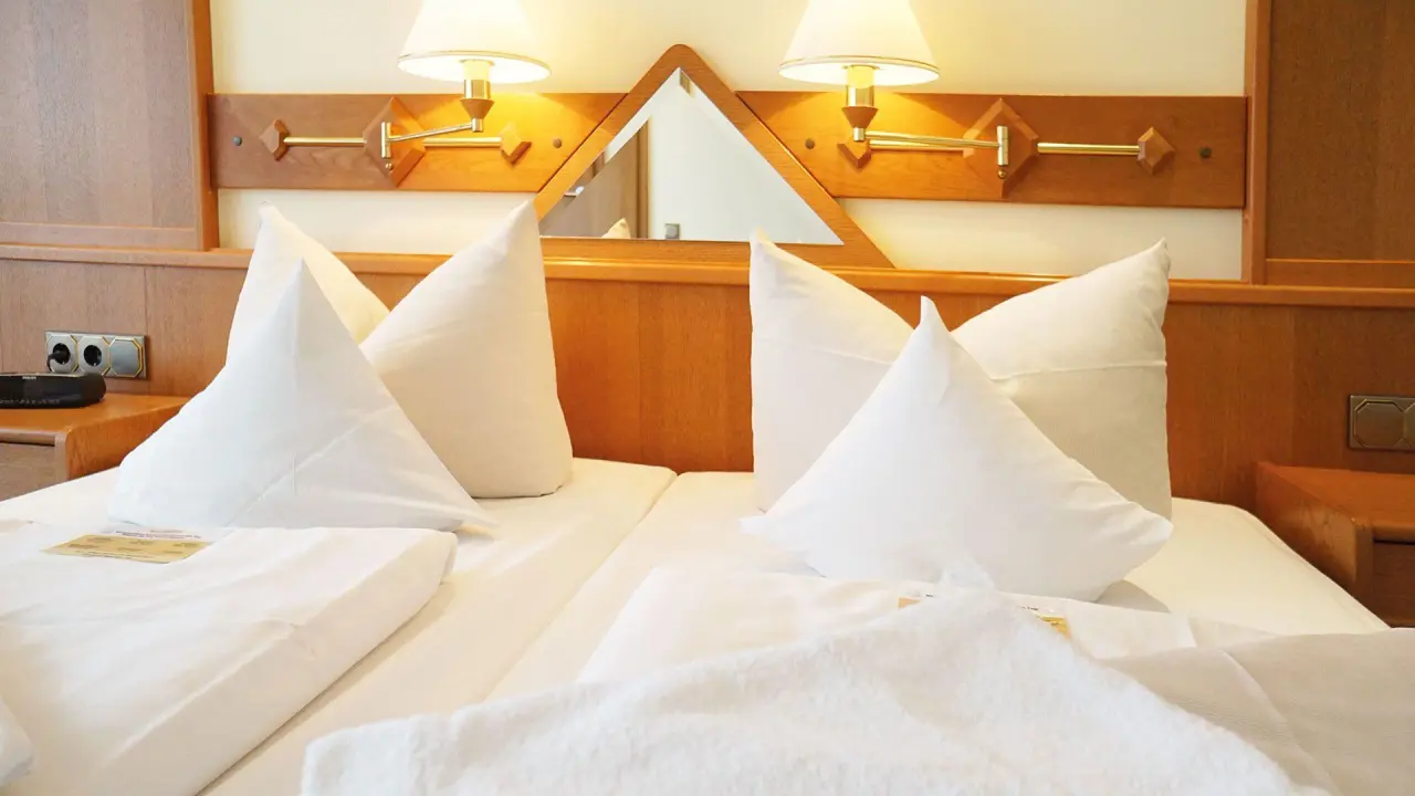 Gemütliches Doppelbett mit weißen Kissen und Holz-Kopfteil im Hotelzimmer des Kurhotel Sonnenhof.