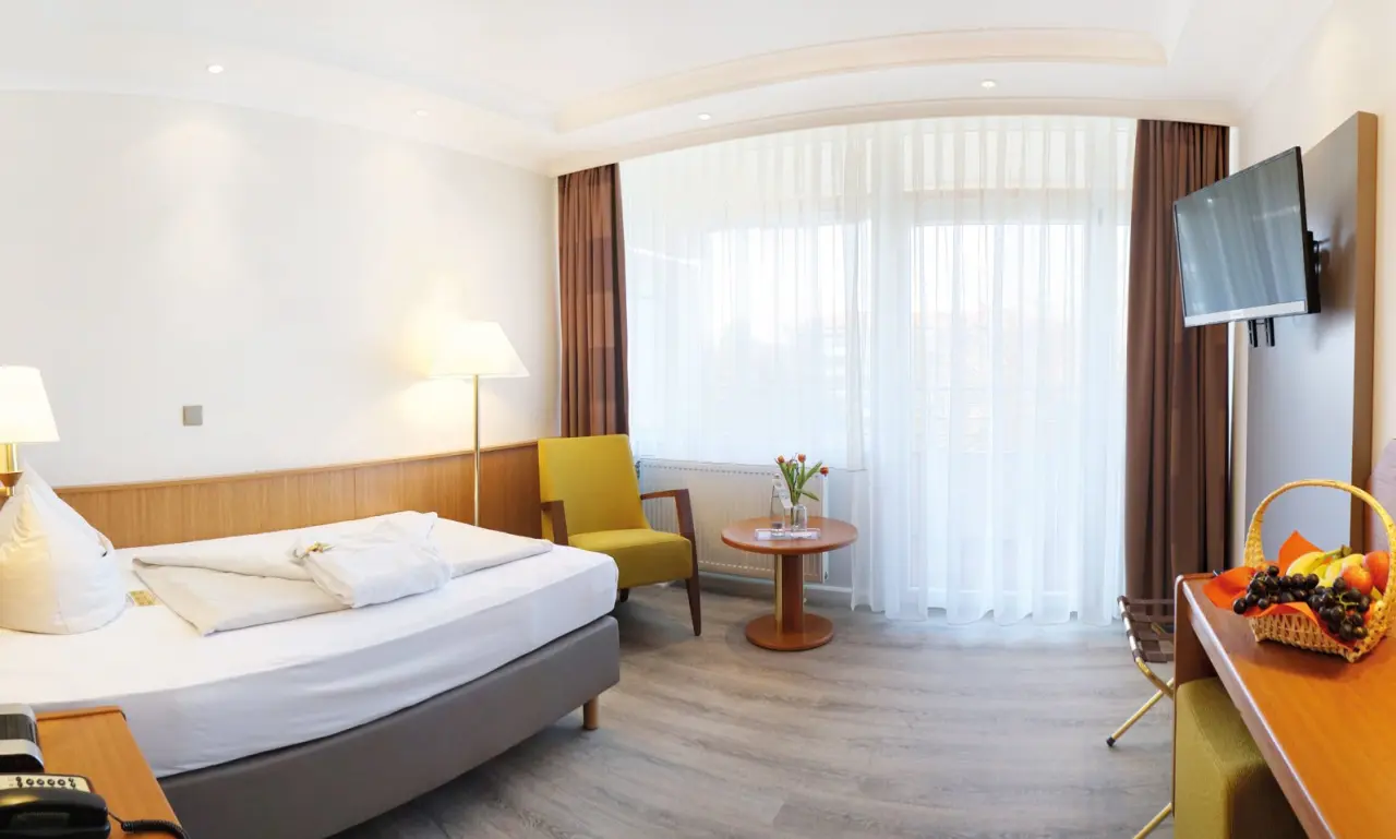 Helles und freundliches Hotelzimmer im Kurhotel Sonnenhof mit Doppelbett, Sessel, TV und Obstkorb.