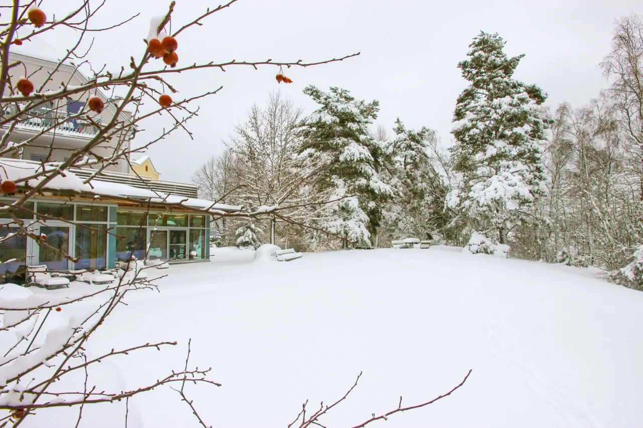 Verschneiter Gartenbereich und Fassade des Gesundheitshotel Klosterberg im Winter.