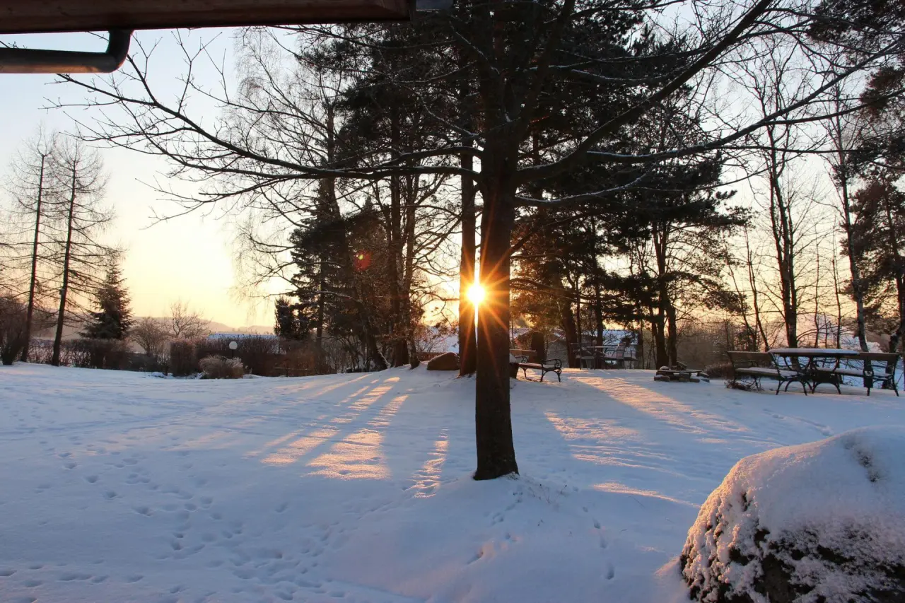 Idyllische Winterlandschaft im Sonnenuntergang mit verschneiten Bäumen und Bänken im Garten des Gesundheitshotels Klosterberg.