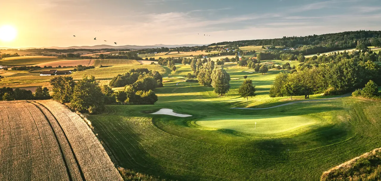 Sonnenuntergang über dem weitläufigen Golfplatz des Quellness & Golf Resort Bad Griesbach mit grünen Fairways und Feldern.