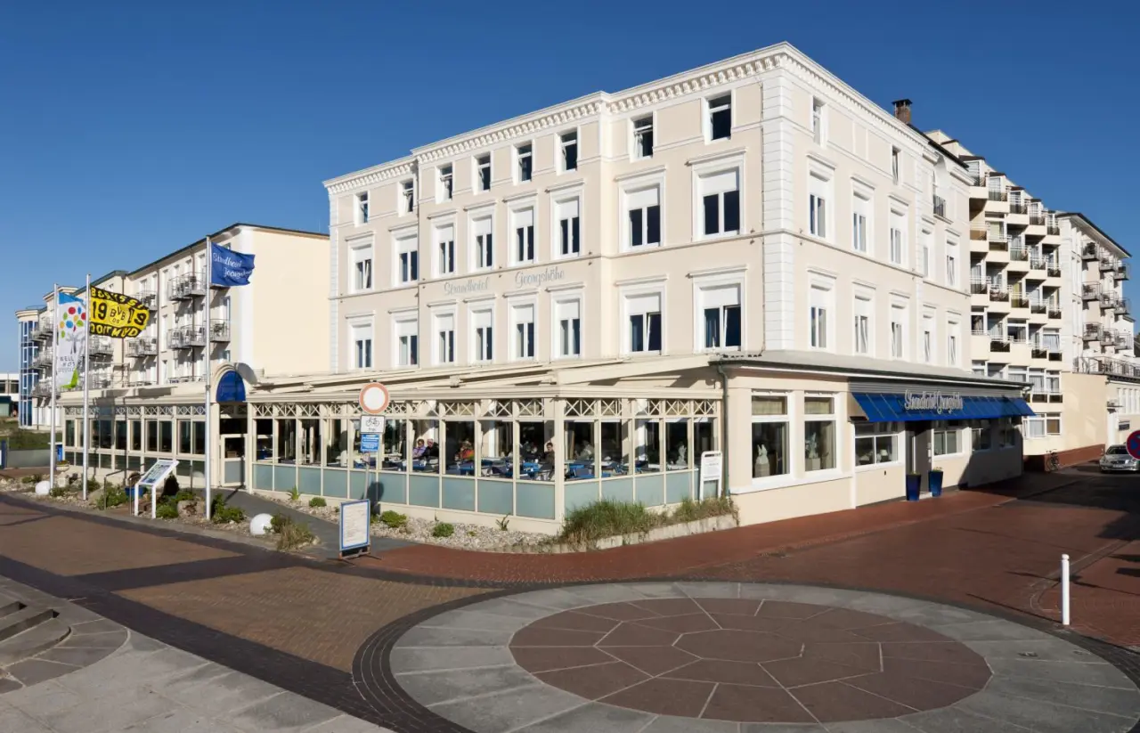 Aussenansicht des Strandhotel Georgshöhe mit heller Fassade, Restaurant und blauem Himmel.