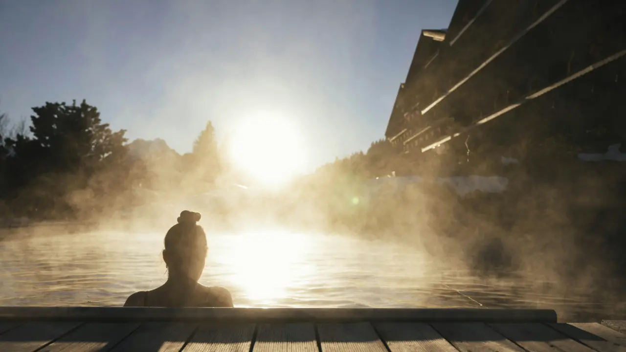 Gast genießt dampfenden Aussenpool des ERMITAGE Wellness- & Spa-Hotels bei Sonnenaufgang mit Bergblick.