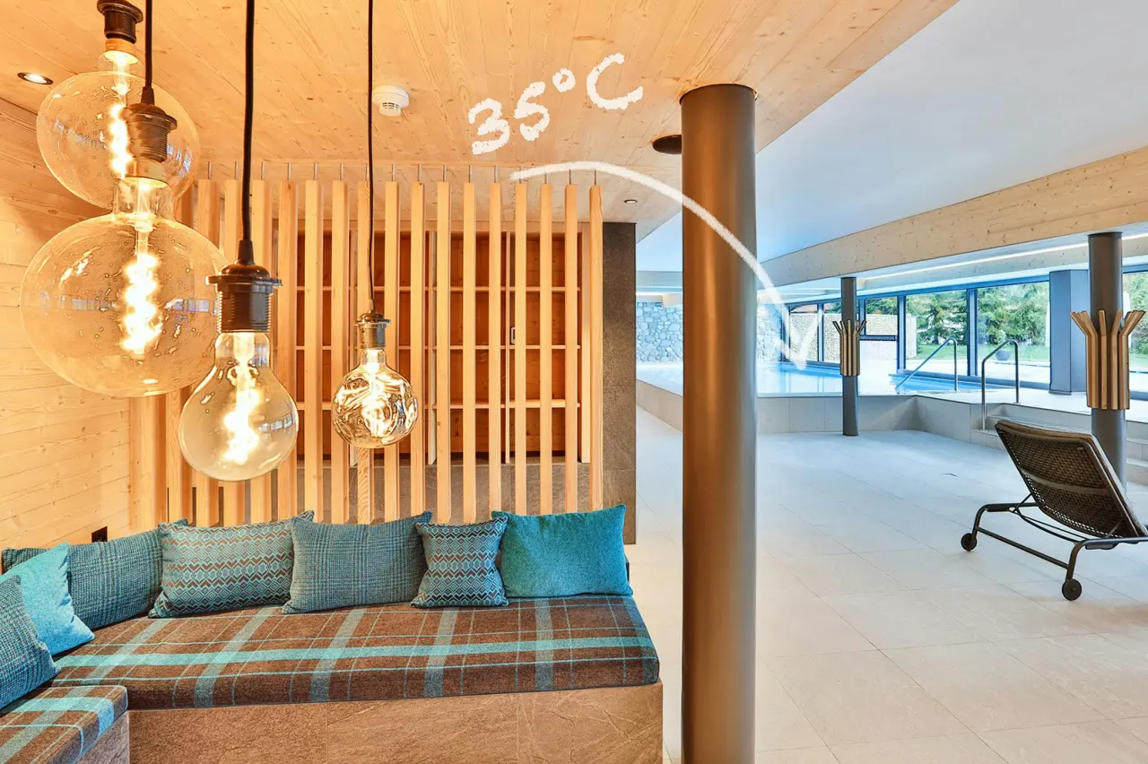 Gemütlicher Ruhebereich mit Holzelementen und Blick auf den warmen Innenpool im ERMITAGE Wellness- & Spa-Hotel.