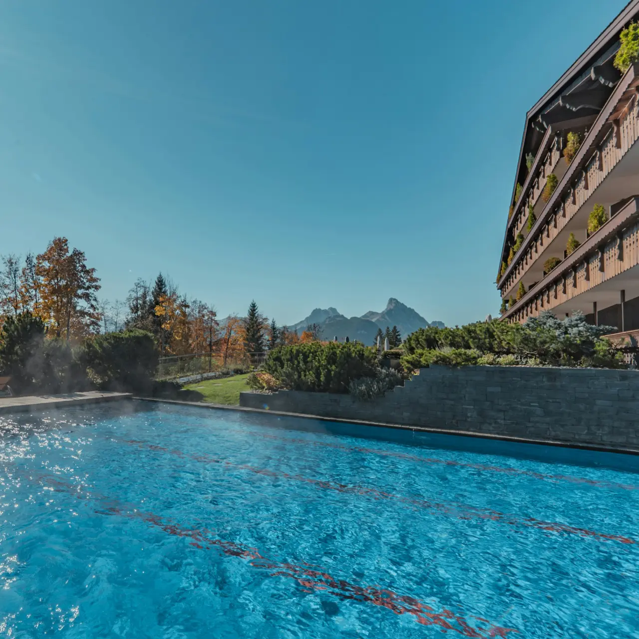 Beheizter Aussenpool mit Bergblick und traditioneller Hotelarchitektur im ERMITAGE Wellness- & Spa-Hotel.