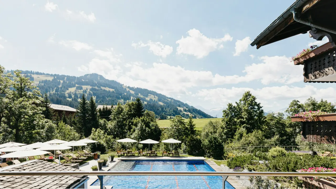 Grosser Aussenpool des ERMITAGE Wellness- & Spa-Hotel mit Liegen, Sonnenschirmen und malerischem Alpenpanorama.