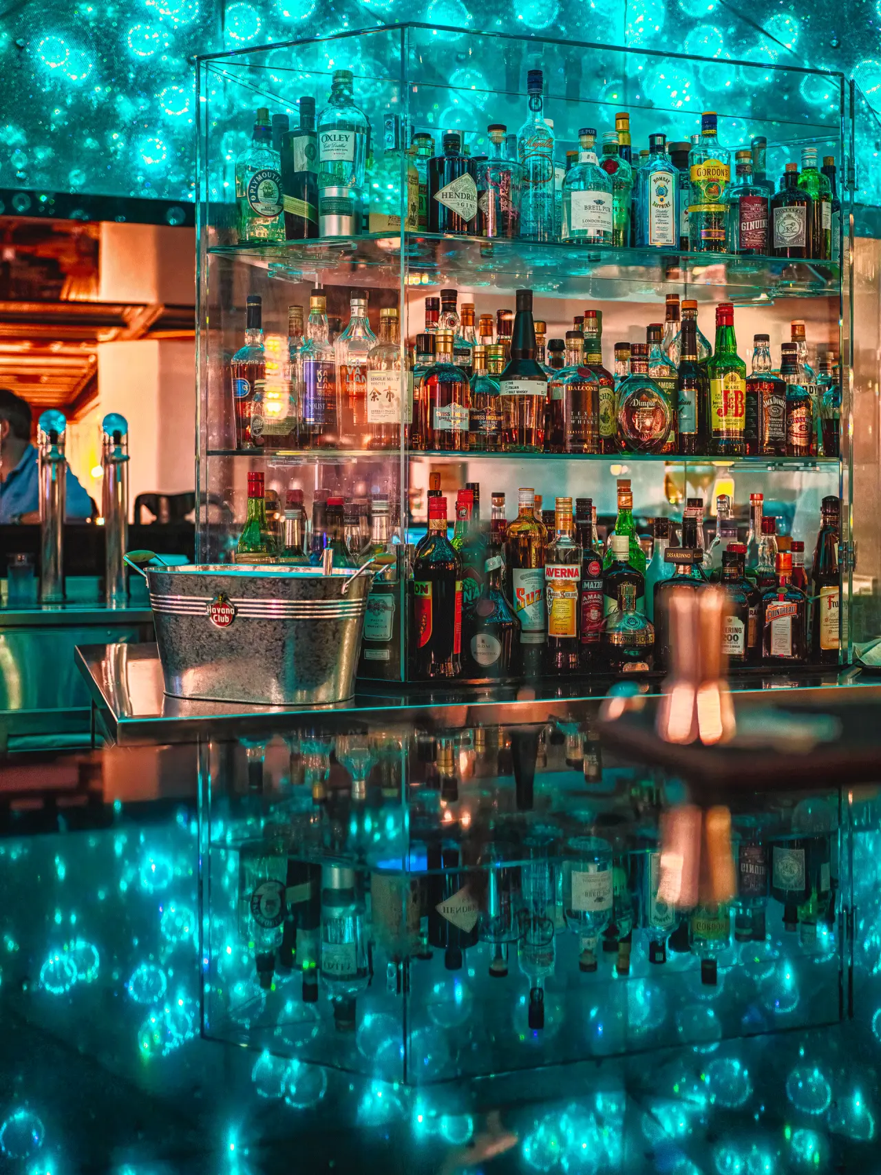 Moderne Hotelbar mit beleuchtetem Spirituosenregal und reflektierender Theke im ERMITAGE Wellness- & Spa-Hotel.
