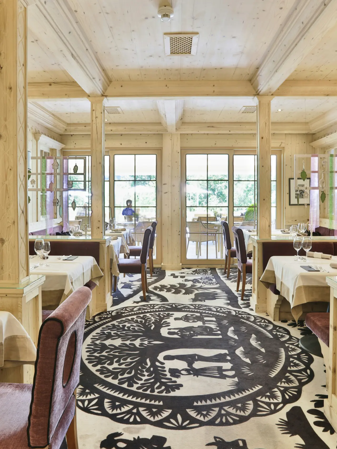 Gemütliches Restaurant mit hellem Holzinterieur, elegant gedeckten Tischen und Blick ins Grüne im ERMITAGE Wellness- & Spa-Hotel.