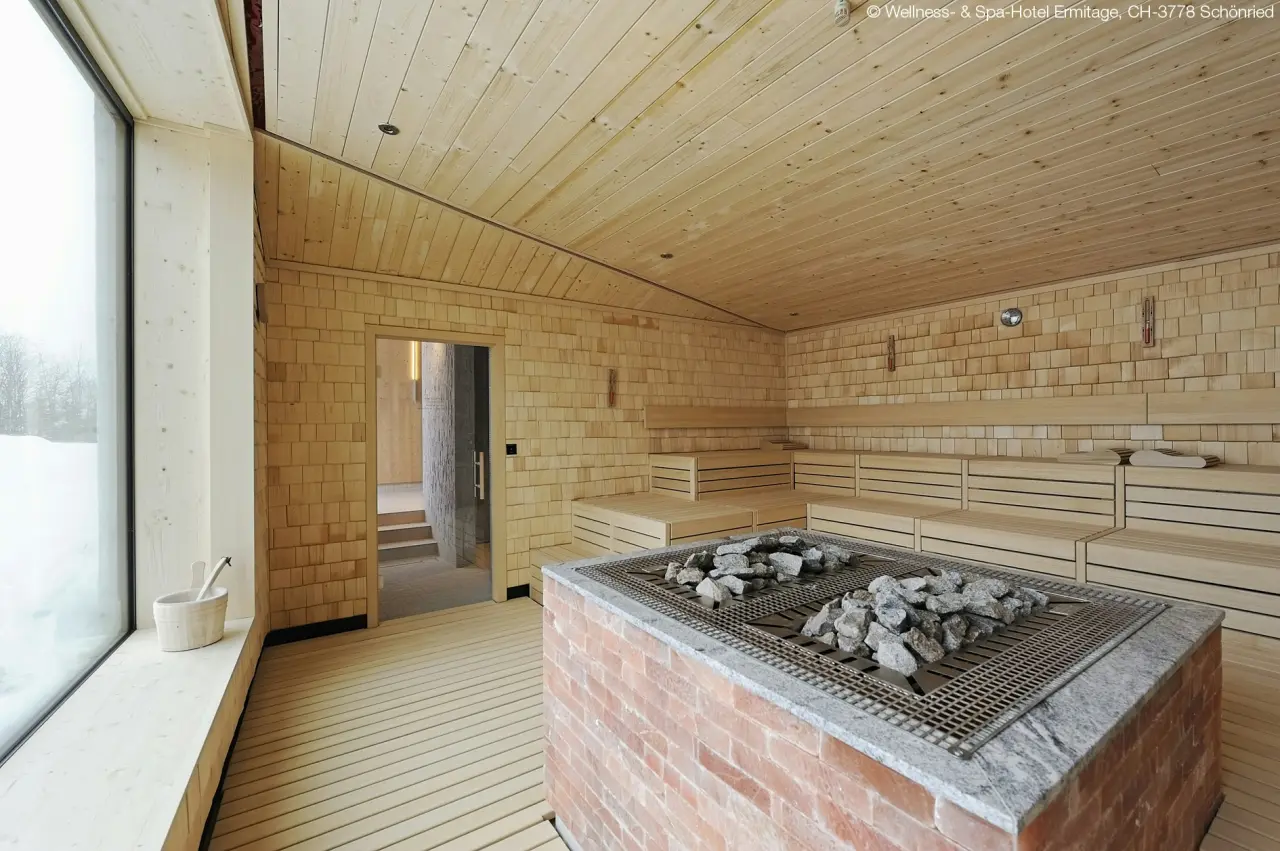 Moderne Holzsauna mit Panoramafenster und Blick auf verschneite Landschaft im ERMITAGE Wellness- & Spa-Hotel.