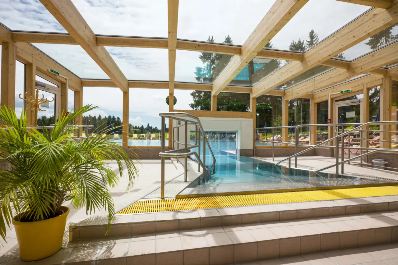 Heller Innenpool mit Holzkonstruktion und Glasdach, verbunden mit dem Aussenbereich im Vivea 4* Hotel Bad Traunstein.