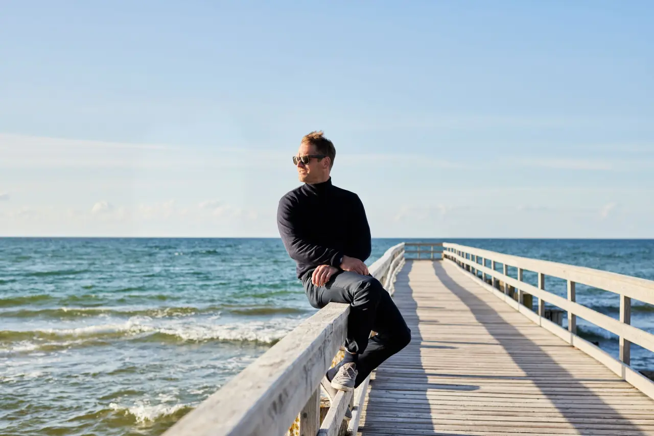 Mann genießt die Ruhe auf der Seebrücke mit Blick auf die Ostsee. Perfekt für einen erholsamen Aufenthalt im Strandhotel Zingst.