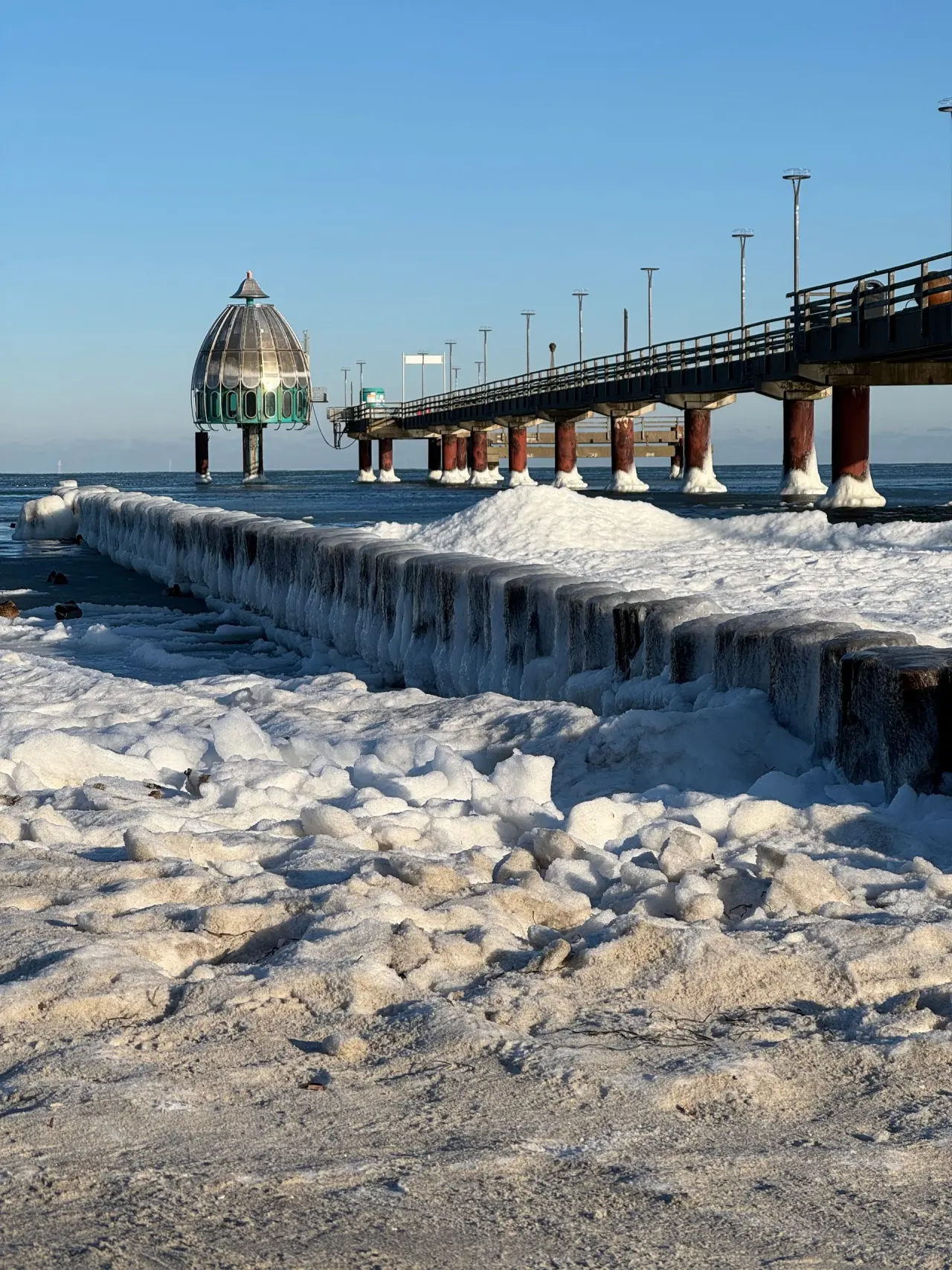 Winterlandschaft am Strandhotel Zingst: Vereiste Seebrücke mit Tauchgondel und gefrorenem Ostseestrand in Zingst.