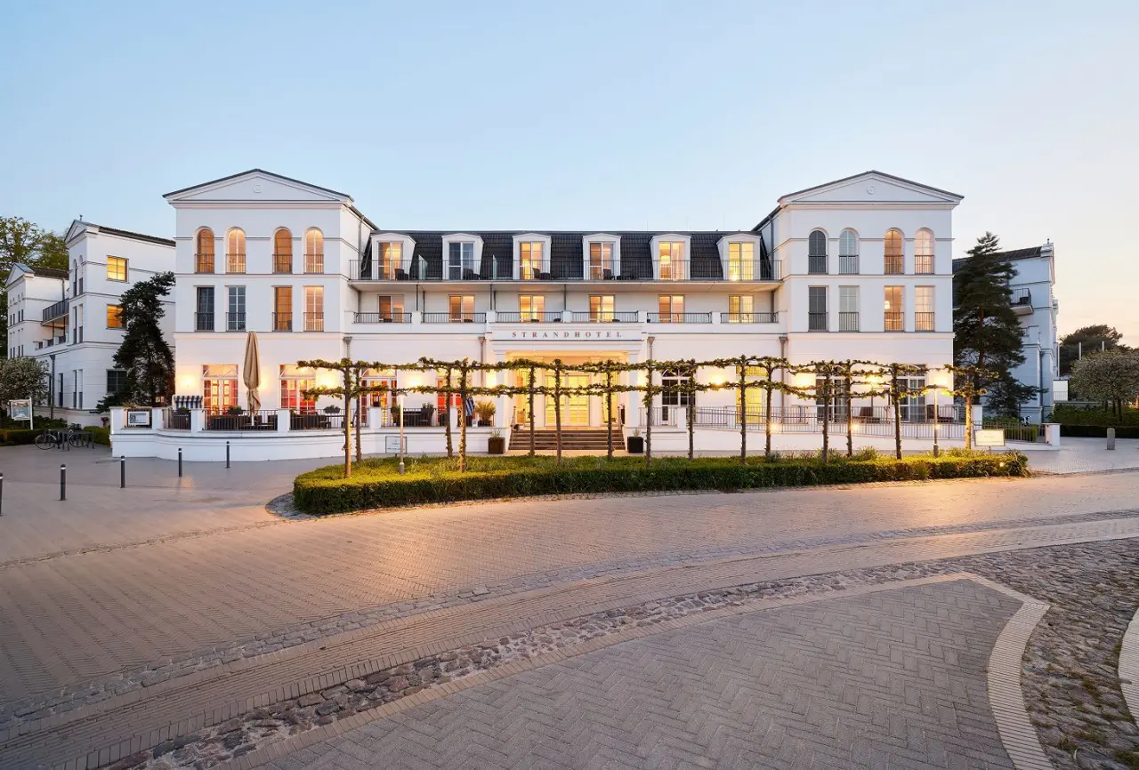 Elegante Aussenansicht des Strandhotel Zingst bei Sonnenuntergang mit beleuchteten Fenstern und Terrasse.