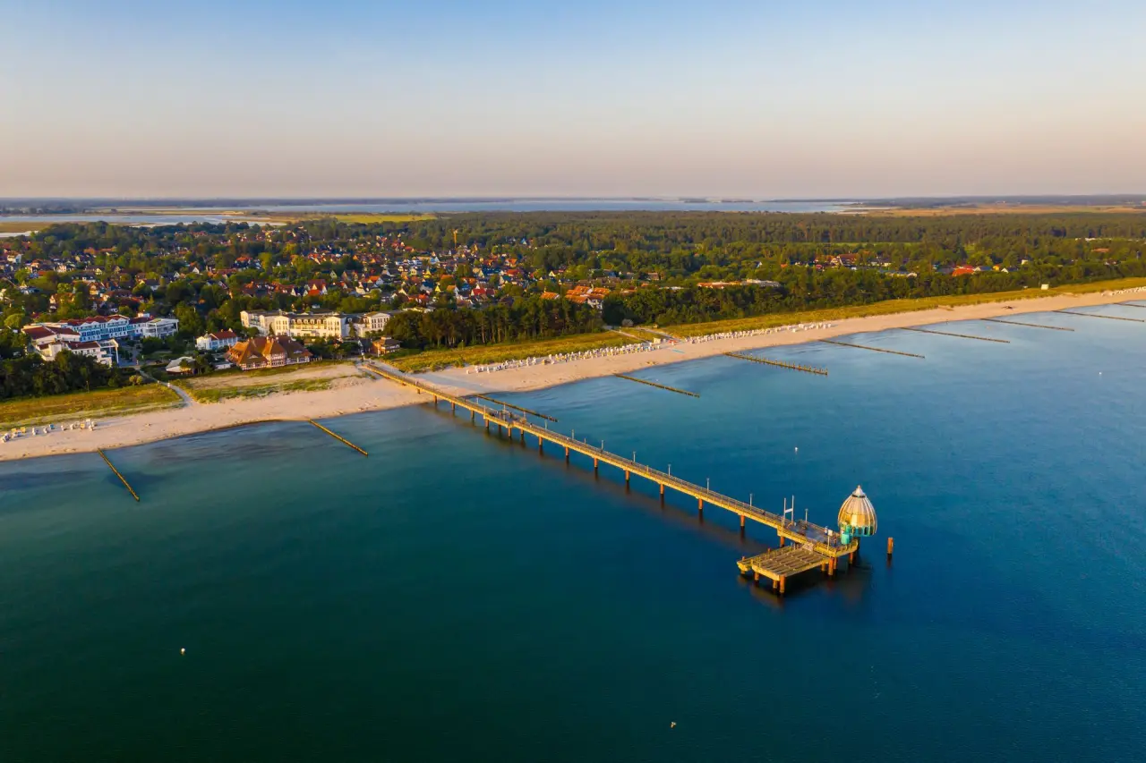 Luftaufnahme des Strandhotels Zingst mit Seebrücke, Sandstrand und Ostsee bei Sonnenuntergang.