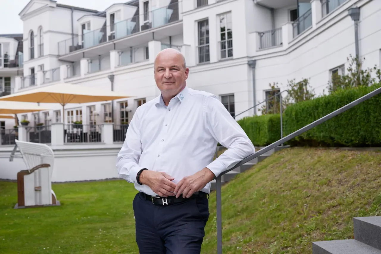 Mann vor der modernen weißen Fassade des Strandhotel Zingst mit Gartenbereich und Strandkorb.