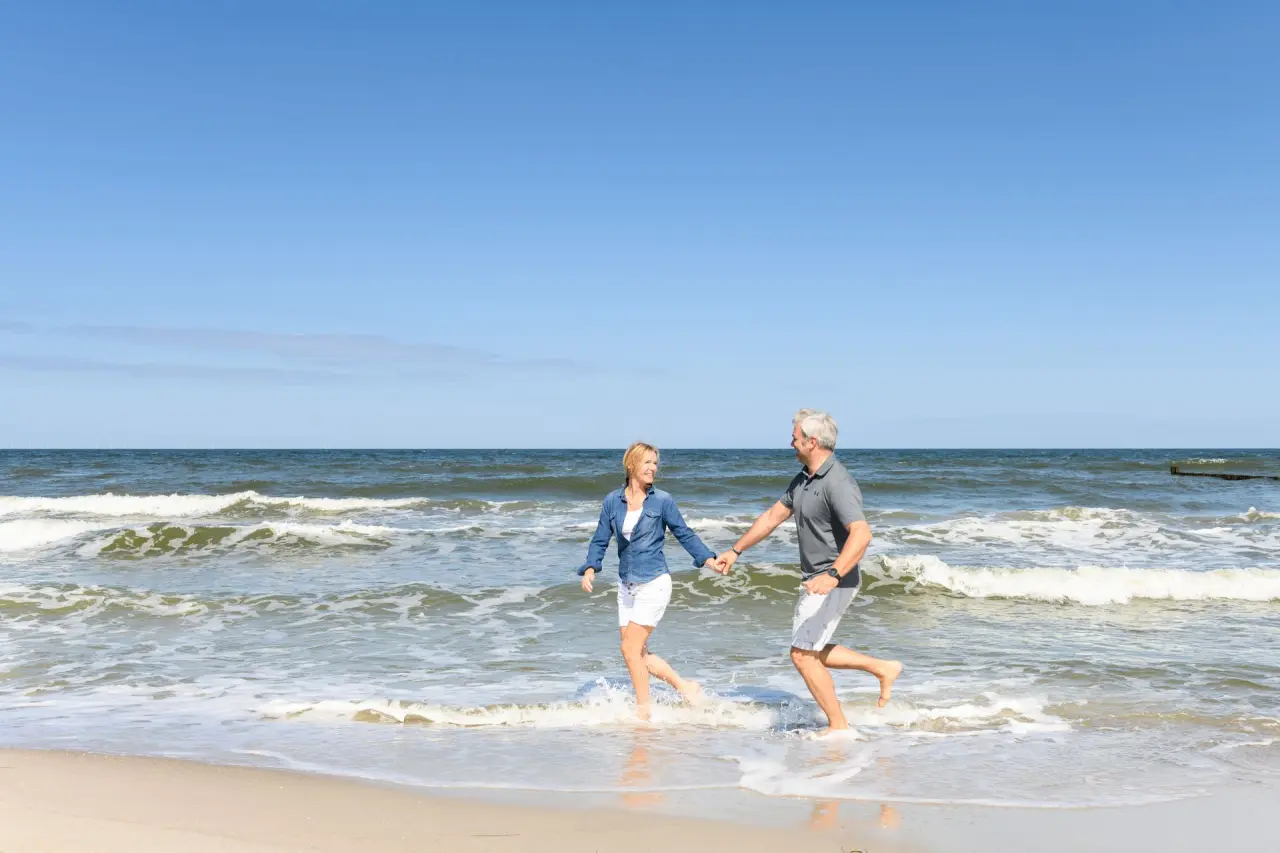 Glückliches Paar läuft Hand in Hand im Meer am Strand von Zingst. Erholsamer Urlaub im Strandhotel Zingst.