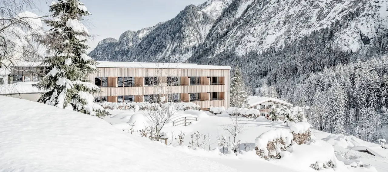 Alpenhotel Zimba im Winter: Modernes Hotelgebäude umgeben von tief verschneiter Alpenlandschaft und Tannenbäumen.