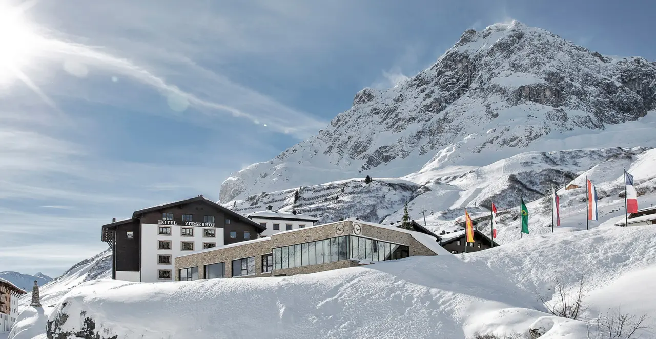 Hotel Zürserhof in verschneiter Alpenlandschaft mit strahlendem Sonnenschein und majestätischem Bergpanorama.