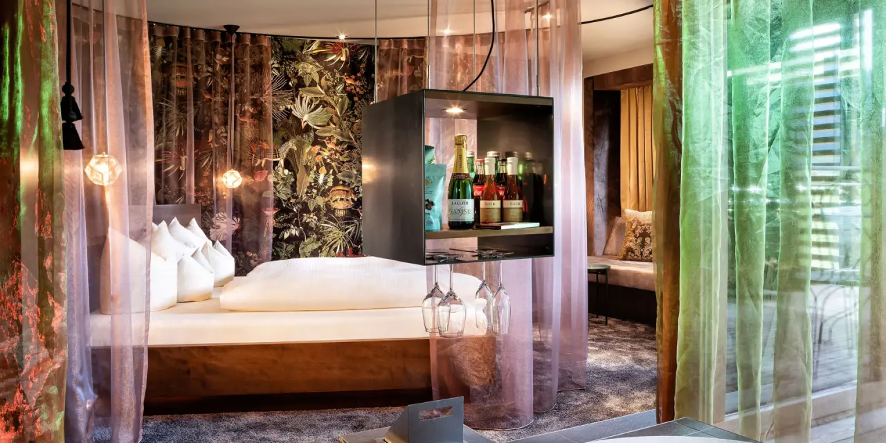 Luxuriöses Hotelzimmer im GAMS zu zweit mit Himmelbett, exotischer Tapete und stilvoller Minibar für romantische Momente.