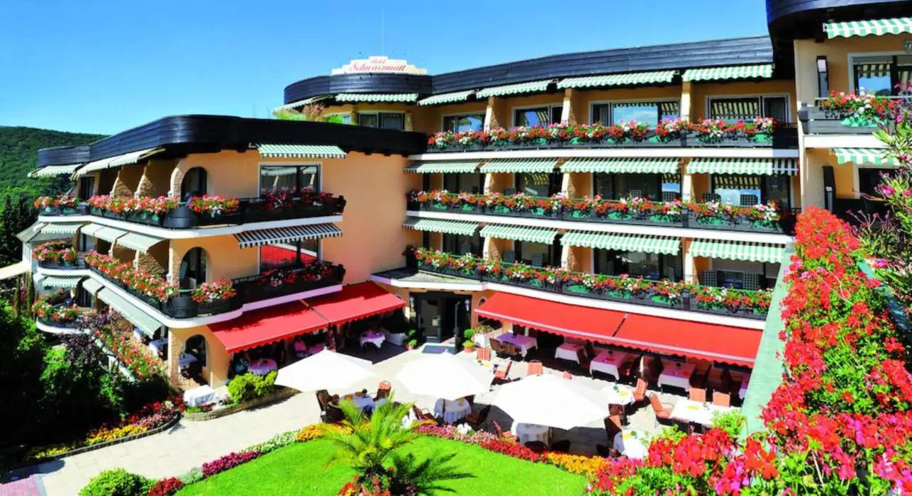 Aussenansicht des Relais & Châteaux Hotel Schwarzmatt mit blühenden Balkonen, grünen Markisen und sonniger Gartenterrasse.