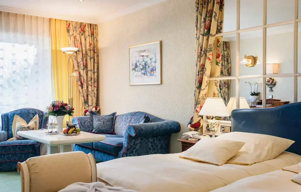 Gemütliches Hotelzimmer im Relais & Châteaux Hotel Schwarzmatt mit Doppelbett, Sitzbereich und floralen Akzenten.
