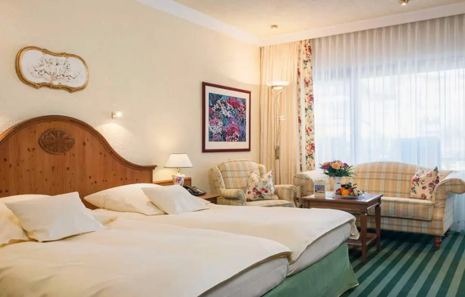 Gemütliches Doppelzimmer mit Sitzecke und floralen Mustern im Relais & Châteaux Hotel Schwarzmatt.