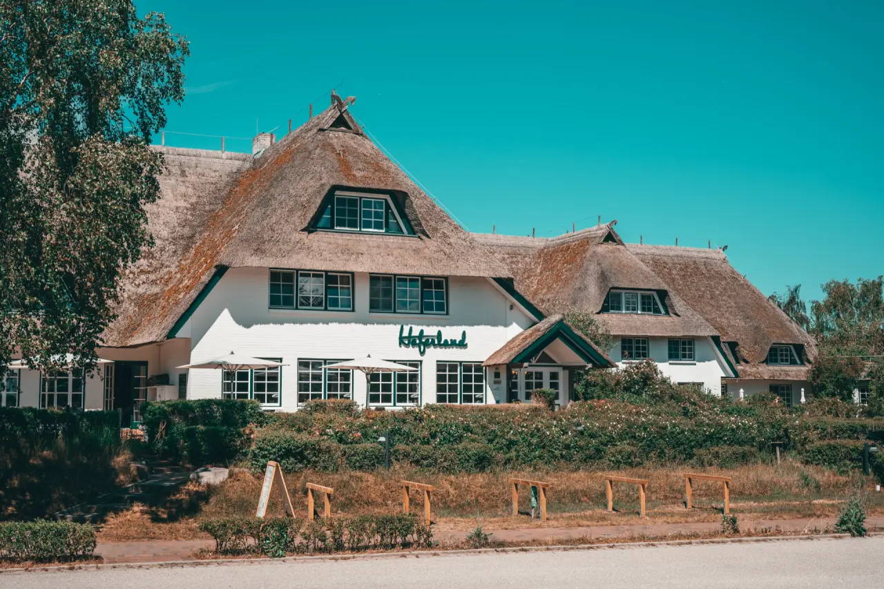 Aussenansicht des Hotel Haferland mit traditionellem Reetdach und weisser Fassade unter blauem Himmel.