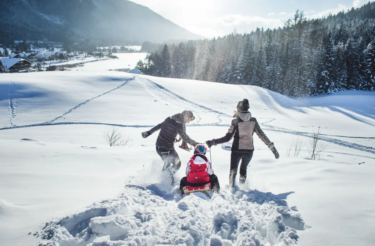 Familie beim Rodeln im tiefen Schnee vor der winterlichen Bergkulisse des Hotel Eden. Aktiver Winterurlaub.