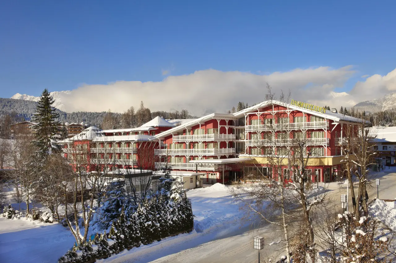 Aussenansicht des Hotel Eden im Winter mit schneebedeckten Bergen und Bäumen unter blauem Himmel.