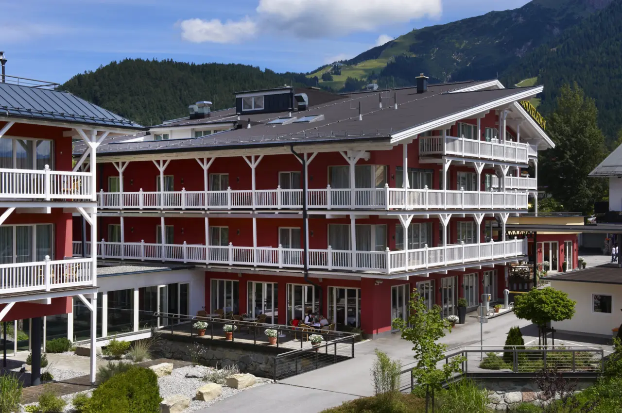 Aussenansicht des Hotel Eden mit roten Fassaden, weissen Balkonen und Bergblick. Alpines Wellnesshotel in den Bergen.
