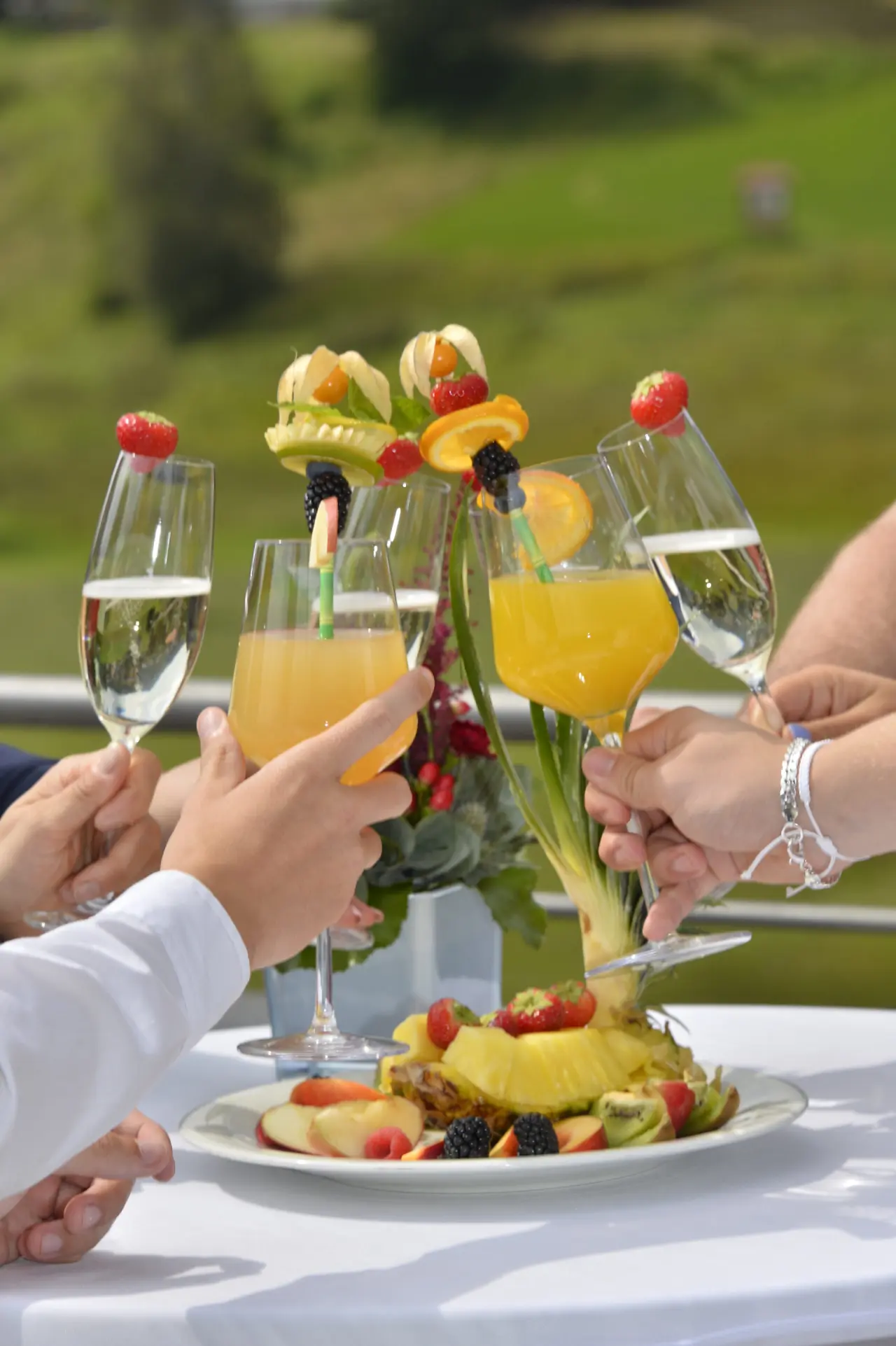 Freunde stoßen mit Sekt und Saft auf der Terrasse des Hotel Eden an, mit frischer Obstplatte.