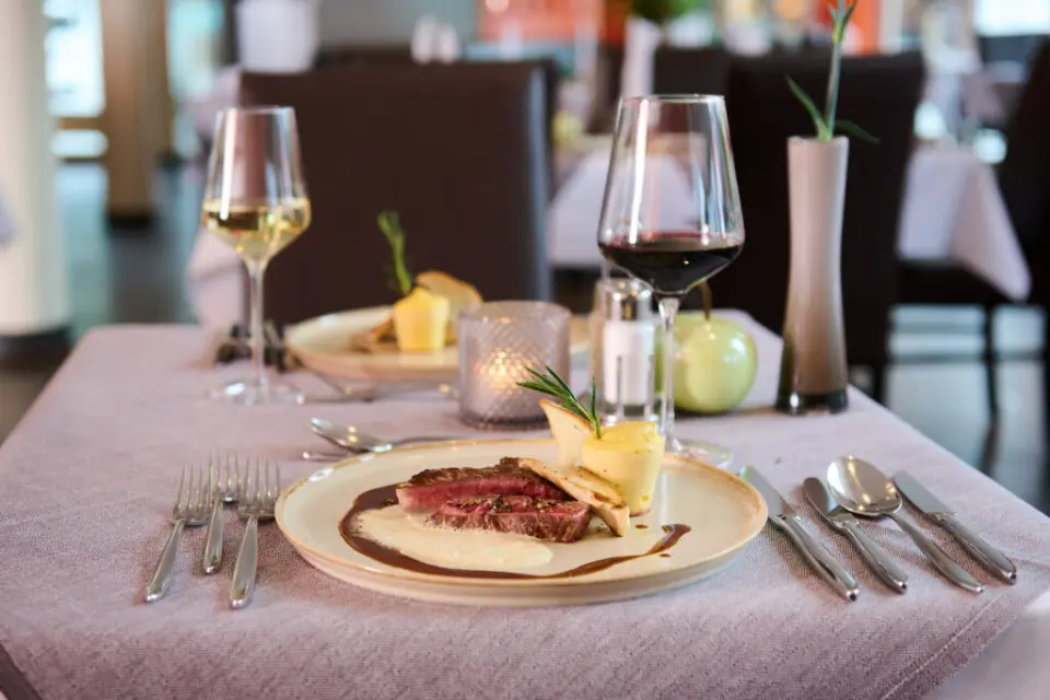 Exquisites Steakgericht mit Beilagen und Weinen im stilvollen Restaurant des Hotel Eden. Perfekt für kulinarische Genussmomente.