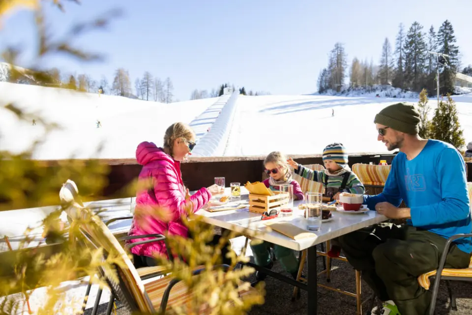 Familie genießt Essen auf der Sonnenterrasse mit Blick auf die Skipiste im Hotel Eden.