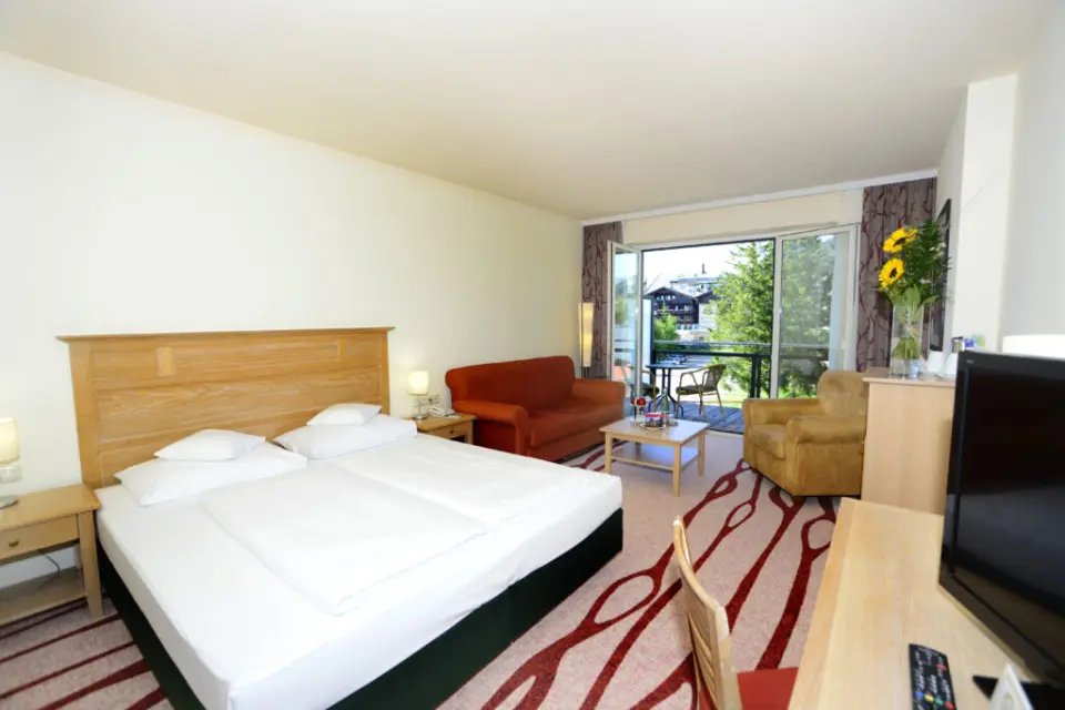 Geräumiges Hotelzimmer im Hotel Eden mit Doppelbett, Sitzbereich und Balkon mit Ausblick.