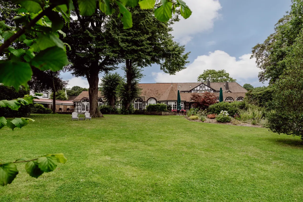 Aussenansicht des Romantik Hotel Bösehof mit weitläufigem grünen Garten, alten Bäumen und charmantem Fachwerkgebäude.