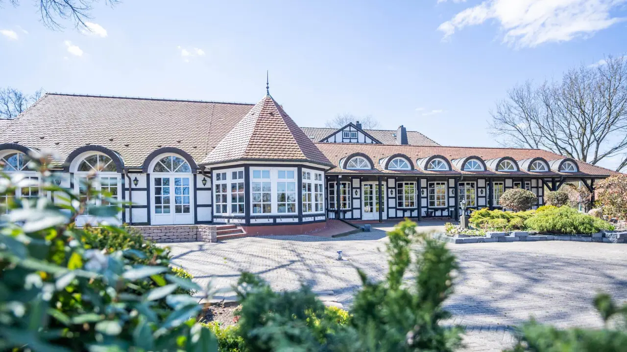 Aussenansicht des Romantik Hotel Bösehof mit Fachwerkfassade, Erker und gepflegtem Vorgarten unter blauem Himmel.