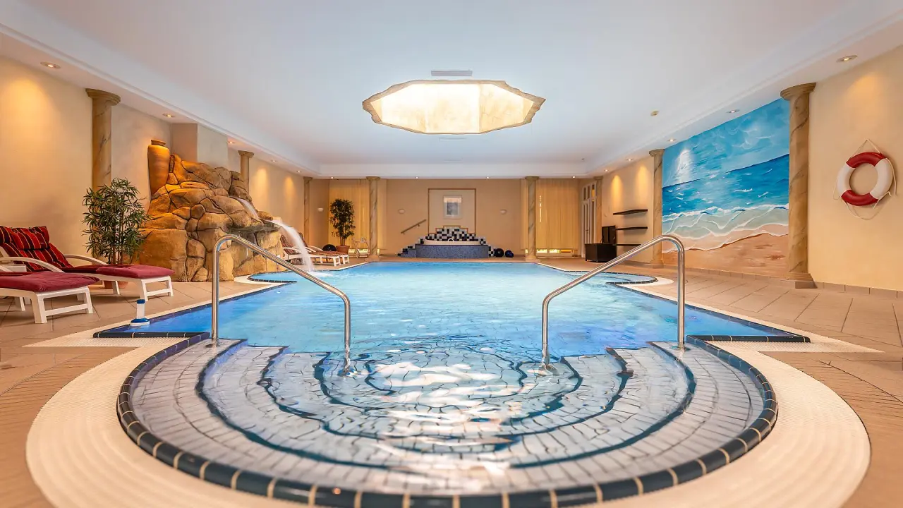 Grosszügiger Innenpool mit Wasserfall, Entspannungsliegen und Wandmalerei im Romantik Hotel Bösehof.