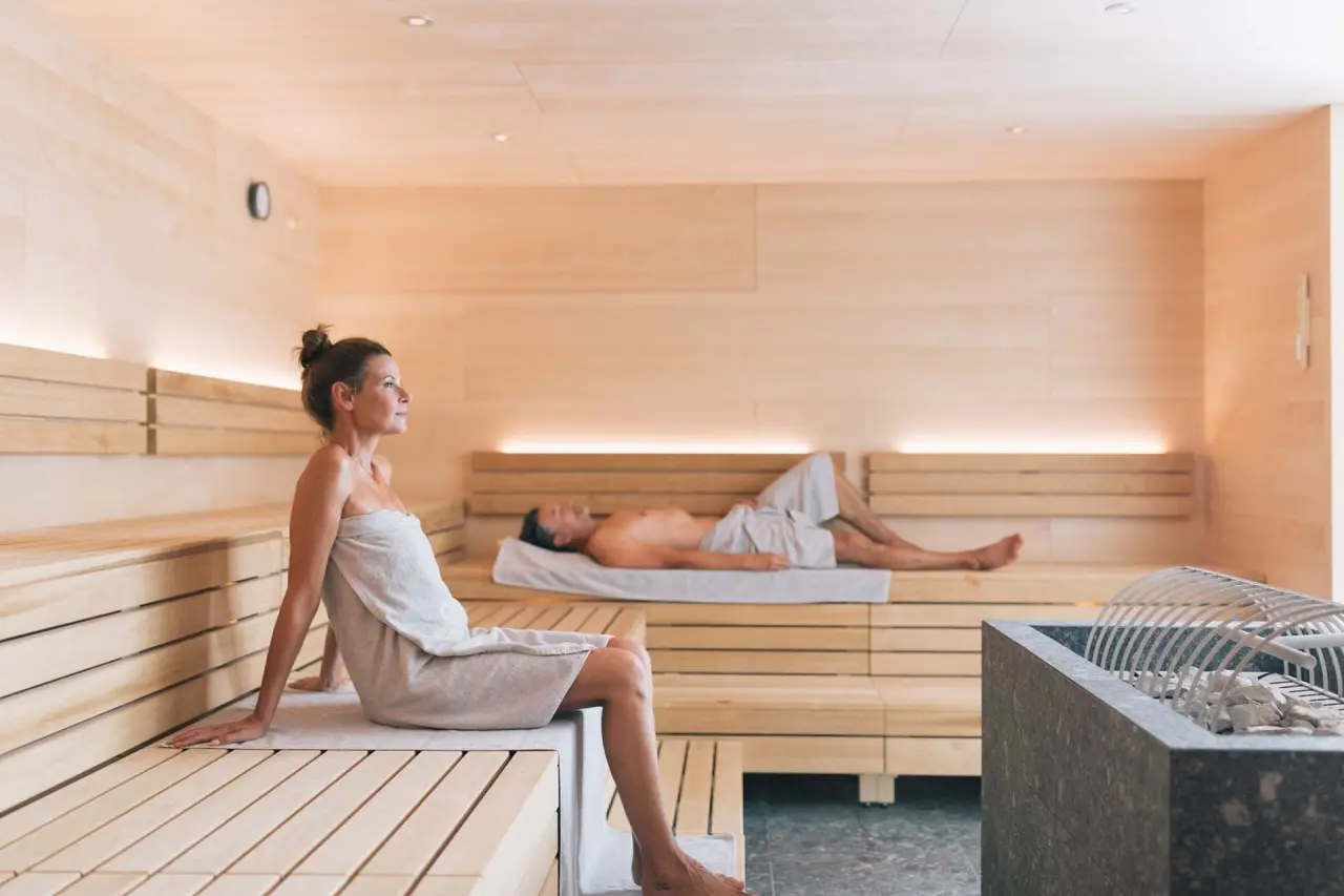 Gäste entspannen in der modernen Holzsauna des Wellnesshotels ...liebes Rot-Flüh mit angenehmer Beleuchtung.