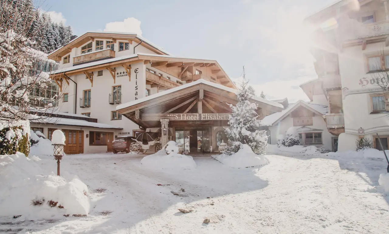 Verschneite Aussenansicht des 4-Sterne Superior Hotel Elisabeth Tirol im Winter mit traditioneller Holzarchitektur.