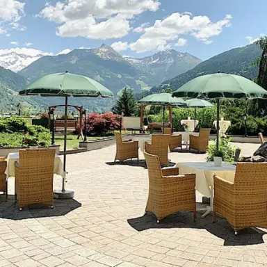 Sonnige Hotelterrasse des sonnenhotel ZUM STERN mit Rattanmöbeln, grünen Sonnenschirmen und Alpenpanorama.