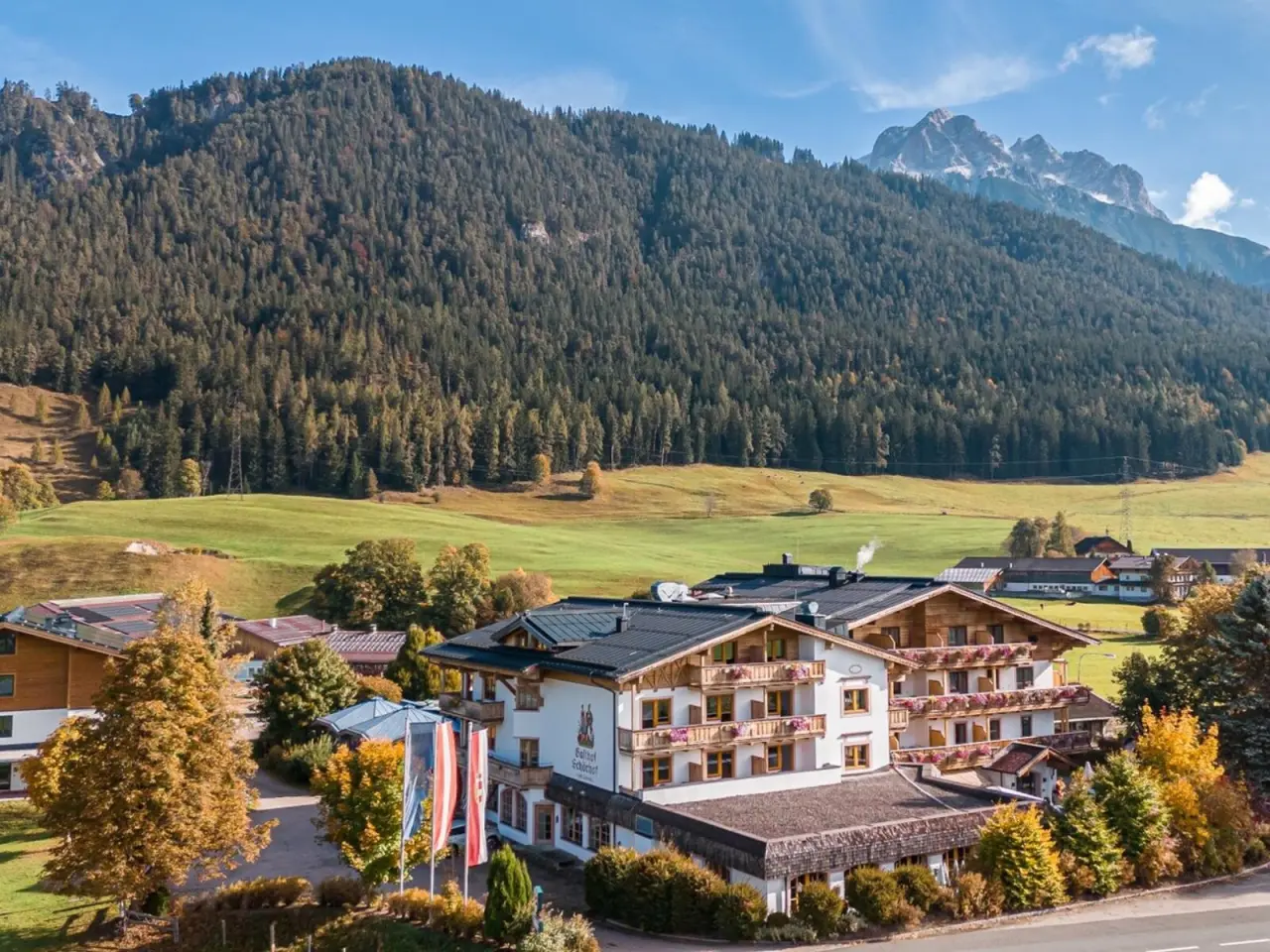 Hotel Schörhof in den österreichischen Alpen. Charmantes Hotelgebäude mit Balkonen, umgeben von grünen Wiesen und Bergen im Herbst.