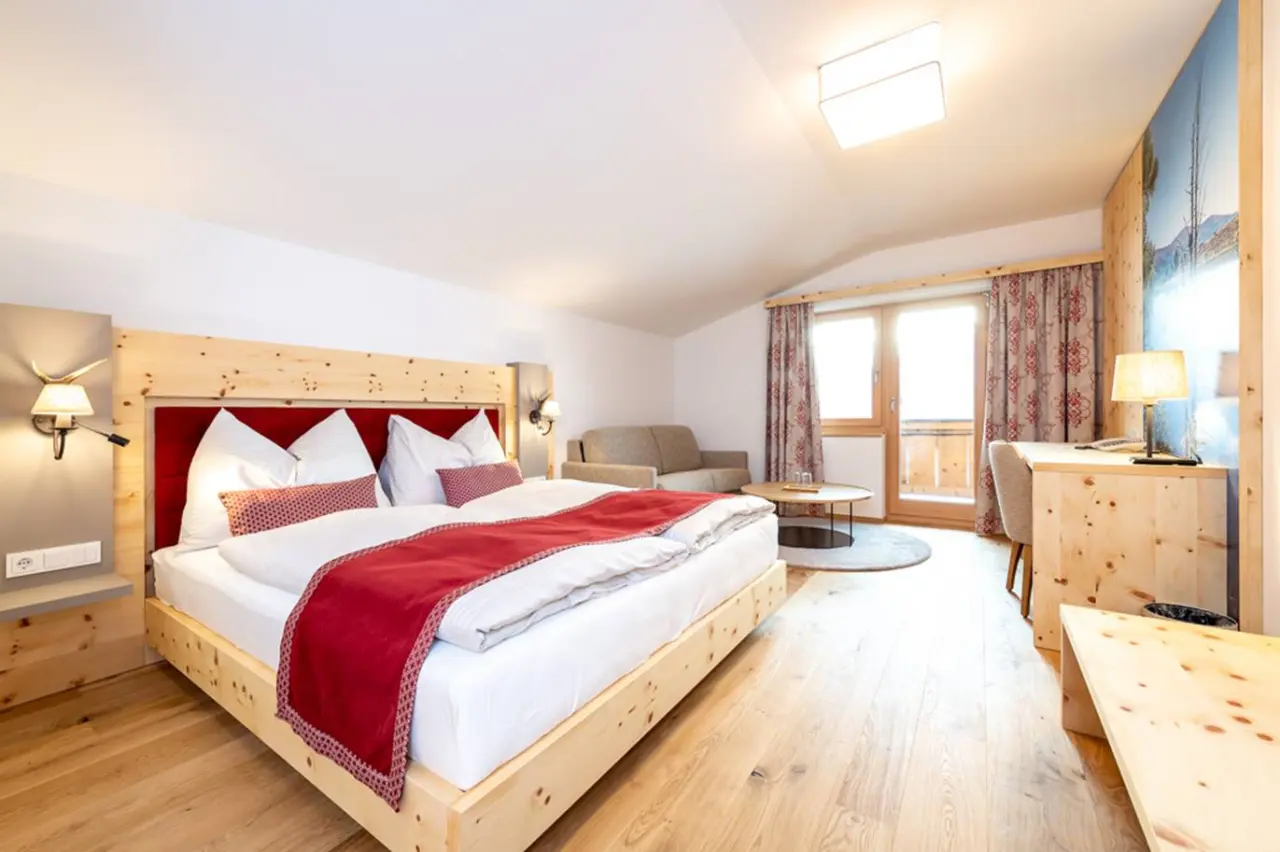 Gemütliches Doppelzimmer im alpinen Stil mit Holzbett, Sofa und Balkon im Hotel Schörhof.