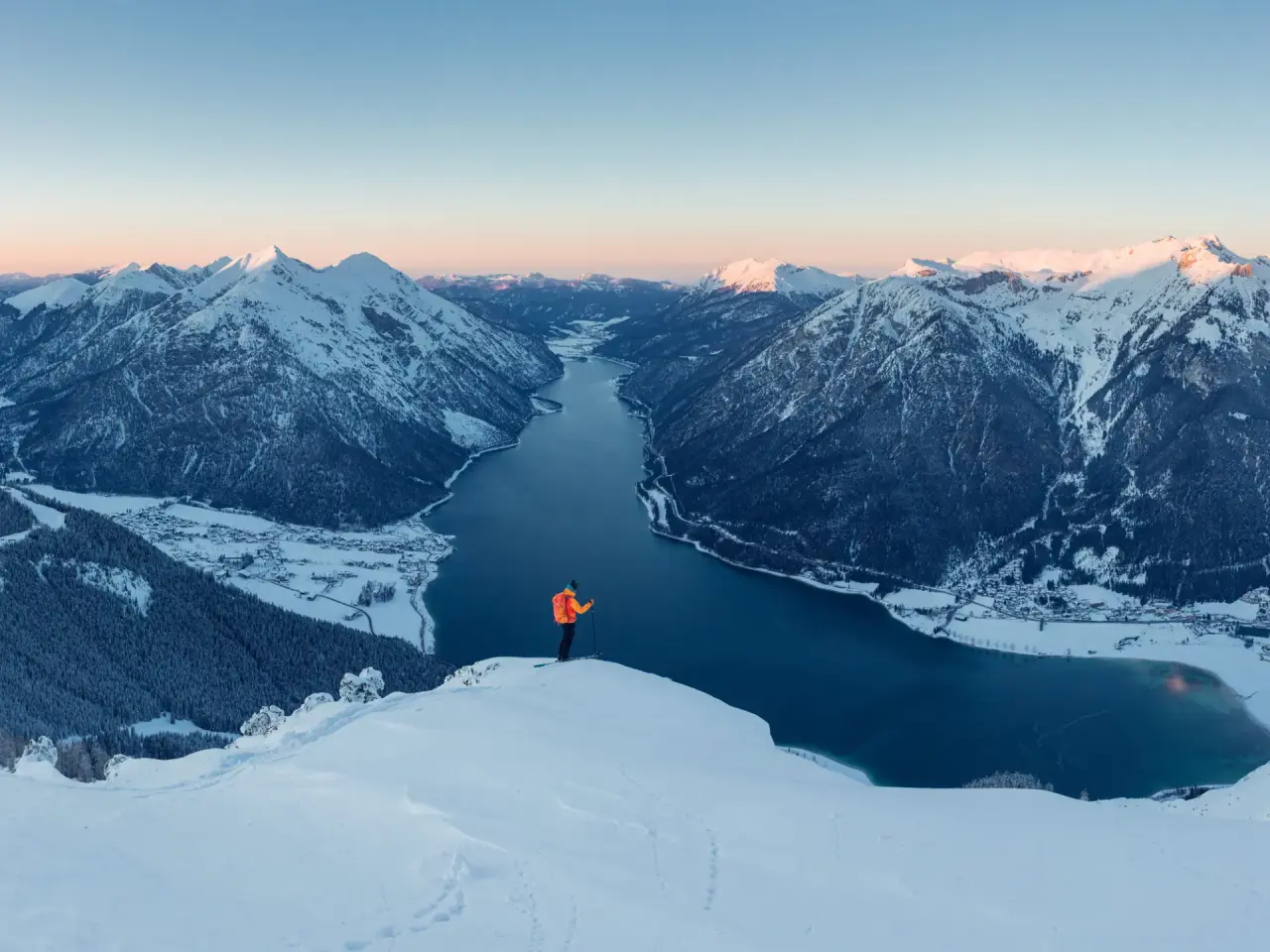 Atemberaubendes Winterpanorama mit verschneiten Bergen, tiefblauem See und Skitourengeher bei Sonnenaufgang, Hotel Vier Jahreszeiten.