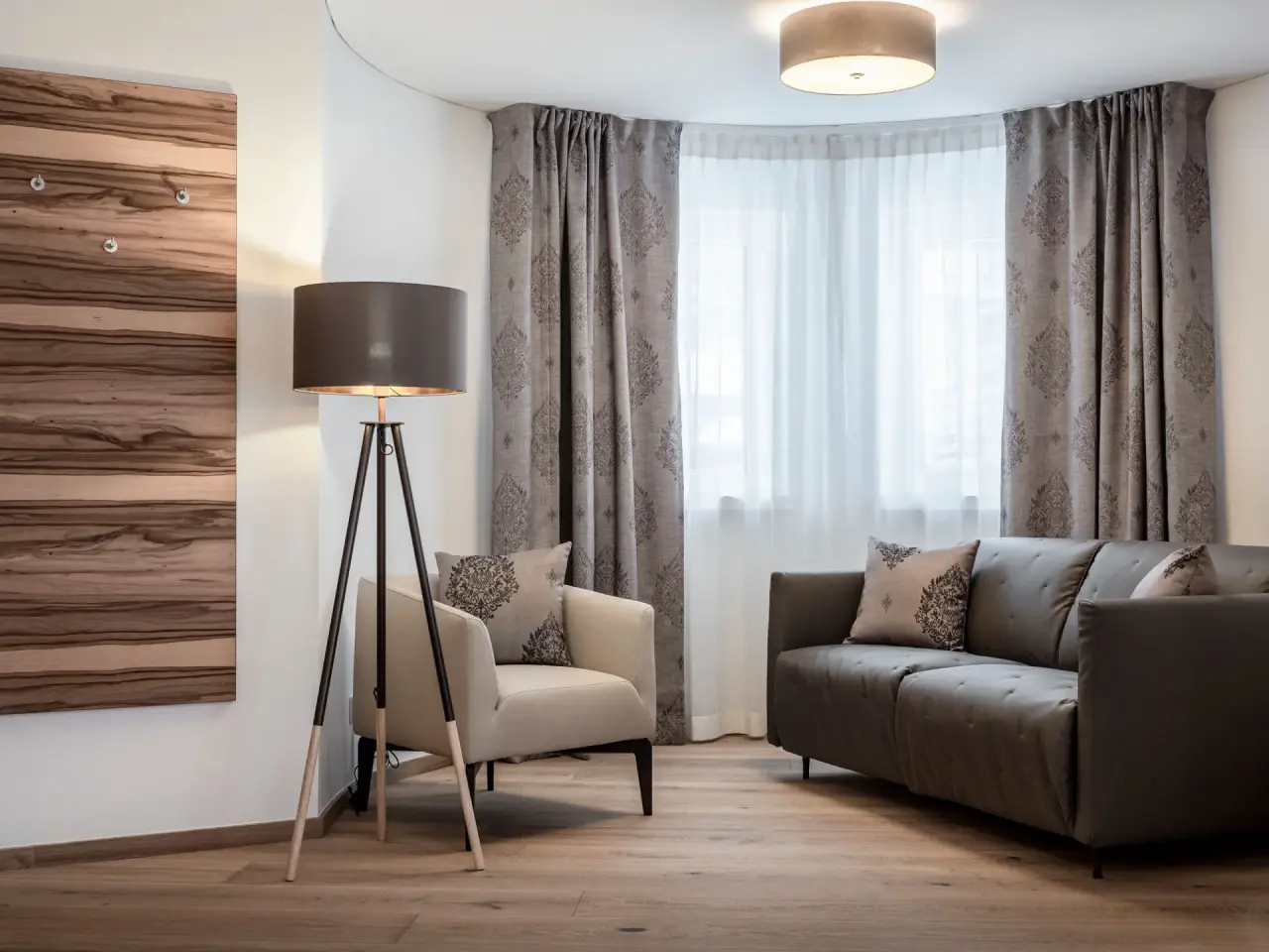 Gemütlicher Wohnbereich in einer Suite des Hotel Vier Jahreszeiten mit Sofa, Sessel, Stehlampe und Holzwand.