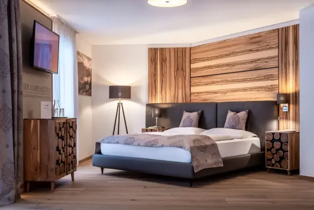 Modernes Doppelzimmer mit Holzelementen und gemütlichem Bett im Hotel Vier Jahreszeiten