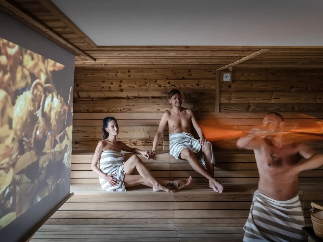 Gäste erleben einen Sauna-Aufguss in der modernen Holzsauna des Hotel Vier Jahreszeiten mit entspannender Projektion.