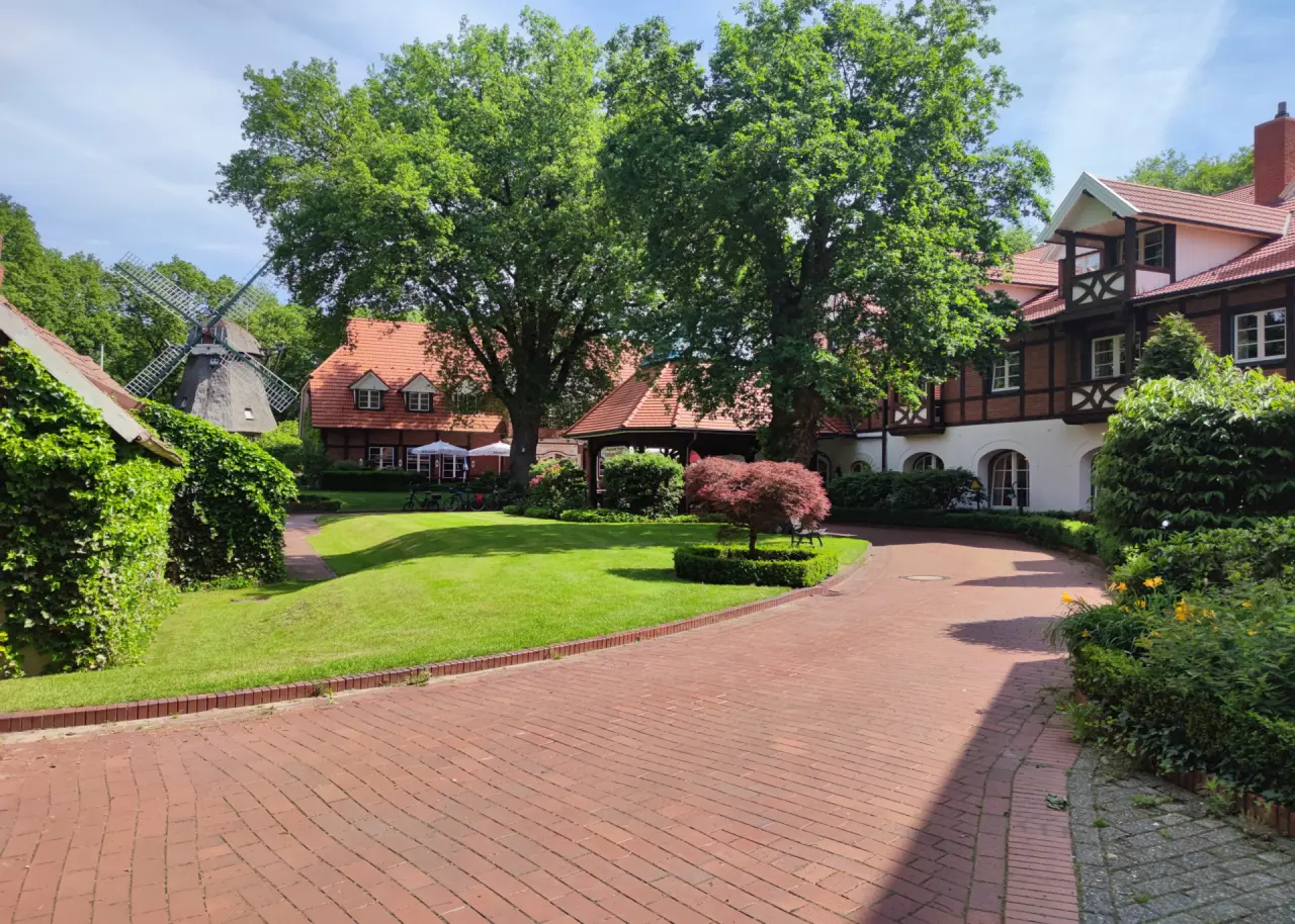 Idyllische Außenansicht des Romantik Hotel Aselager Mühle mit historischer Windmühle, gepflegtem Garten und charmanten Gebäuden.