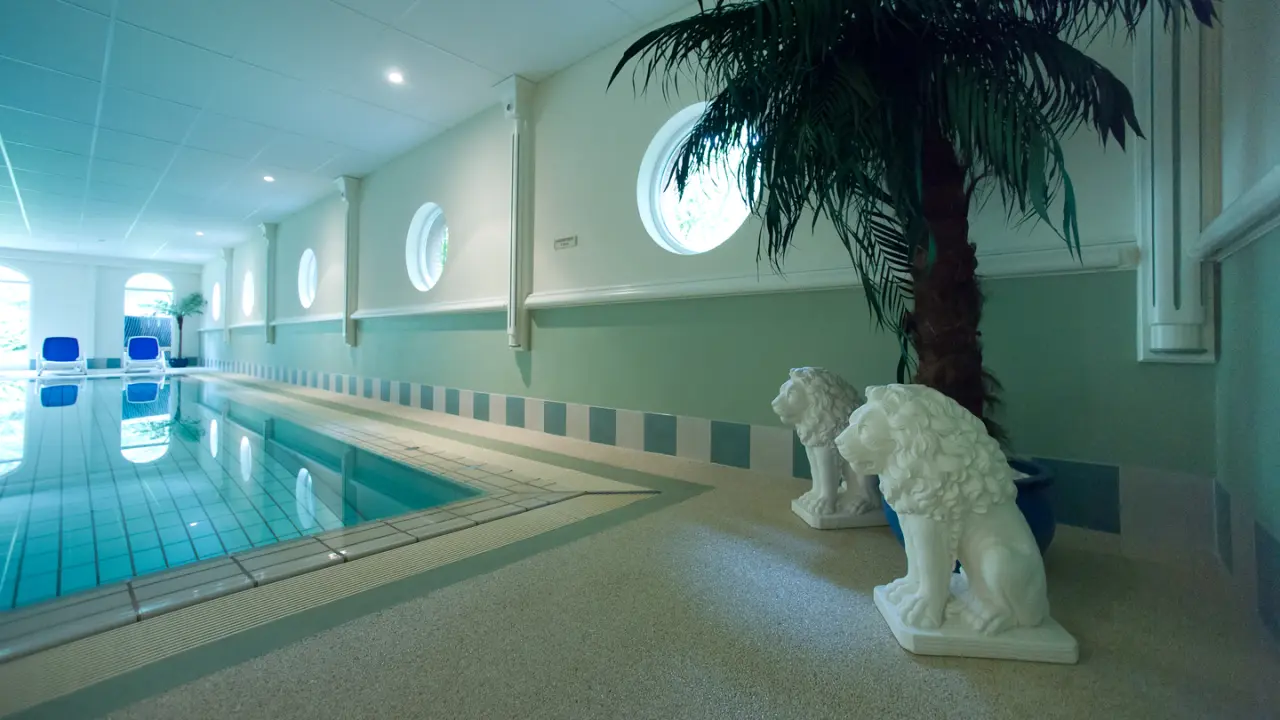 Innenpool im Romantik Hotel Aselager Mühle mit Liegestühlen, runden Fenstern und dekorativen Löwenstatuen.