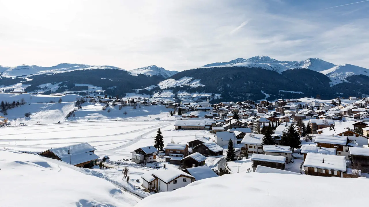 Idyllisches, verschneites Bergdorf mit traditionellen Häusern und majestätischem Alpenpanorama im Winter, La Val Hotel & Spa.